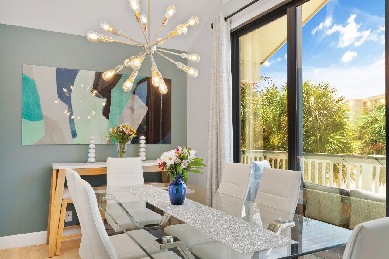 Un espace repas moderne avec une table en verre, des chaises blanches, un vase bleu orné de fleurs et un luminaire contemporain.