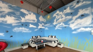 A room with a mural of a sky and clouds, a white sofa, a glass coffee table, and a red chair. - OYO 1228 Gia Hoang Homestay (Xuan Huong - Da Lat)