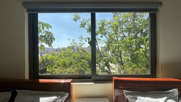 A room with two beds, a window, and a view of trees and buildings. - OYO 1228 Gia Hoang Homestay (Xuan Huong - Da Lat)