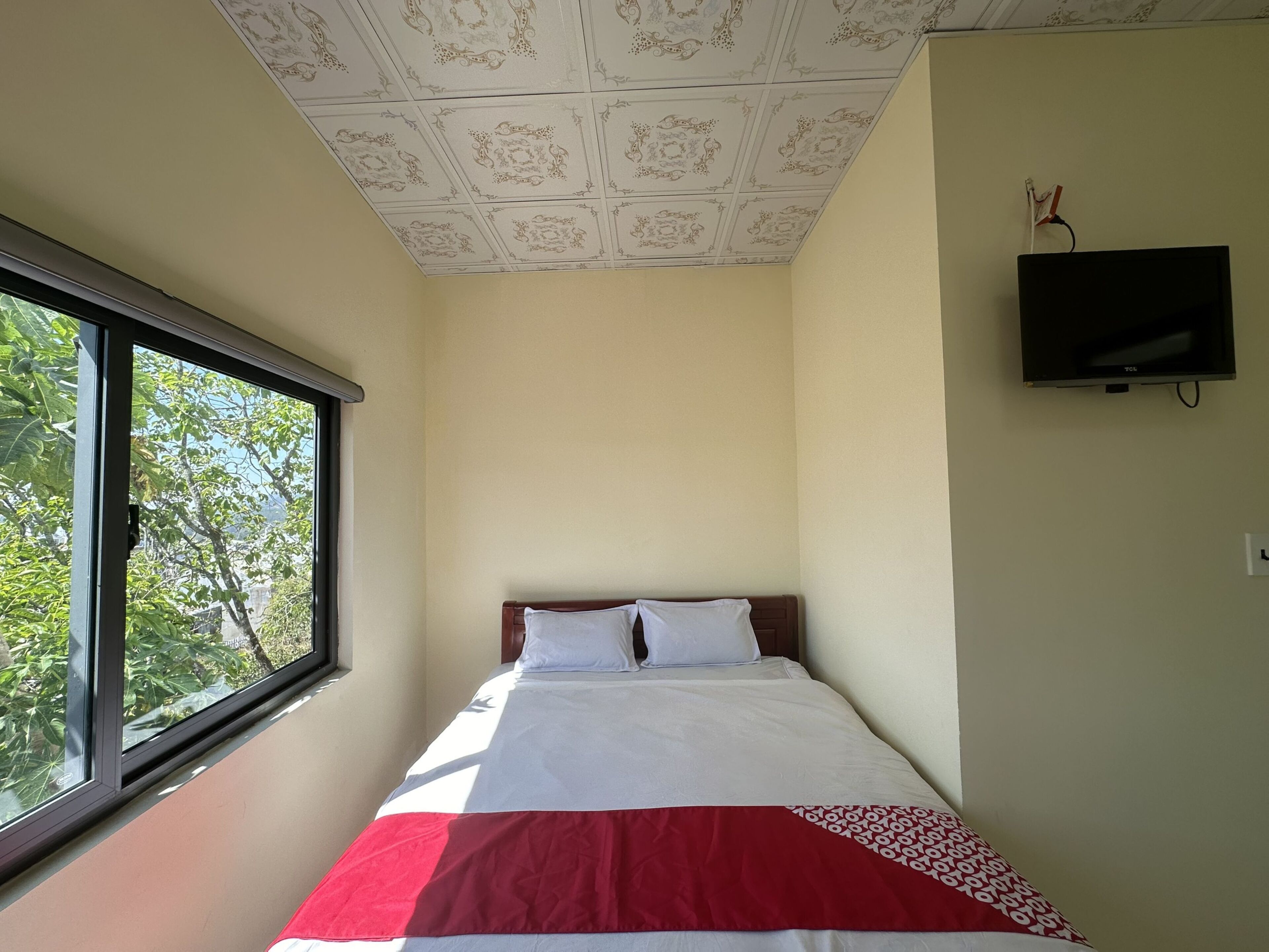 Un dormitorio con una cama, una ventana, un televisor y un techo estampado.