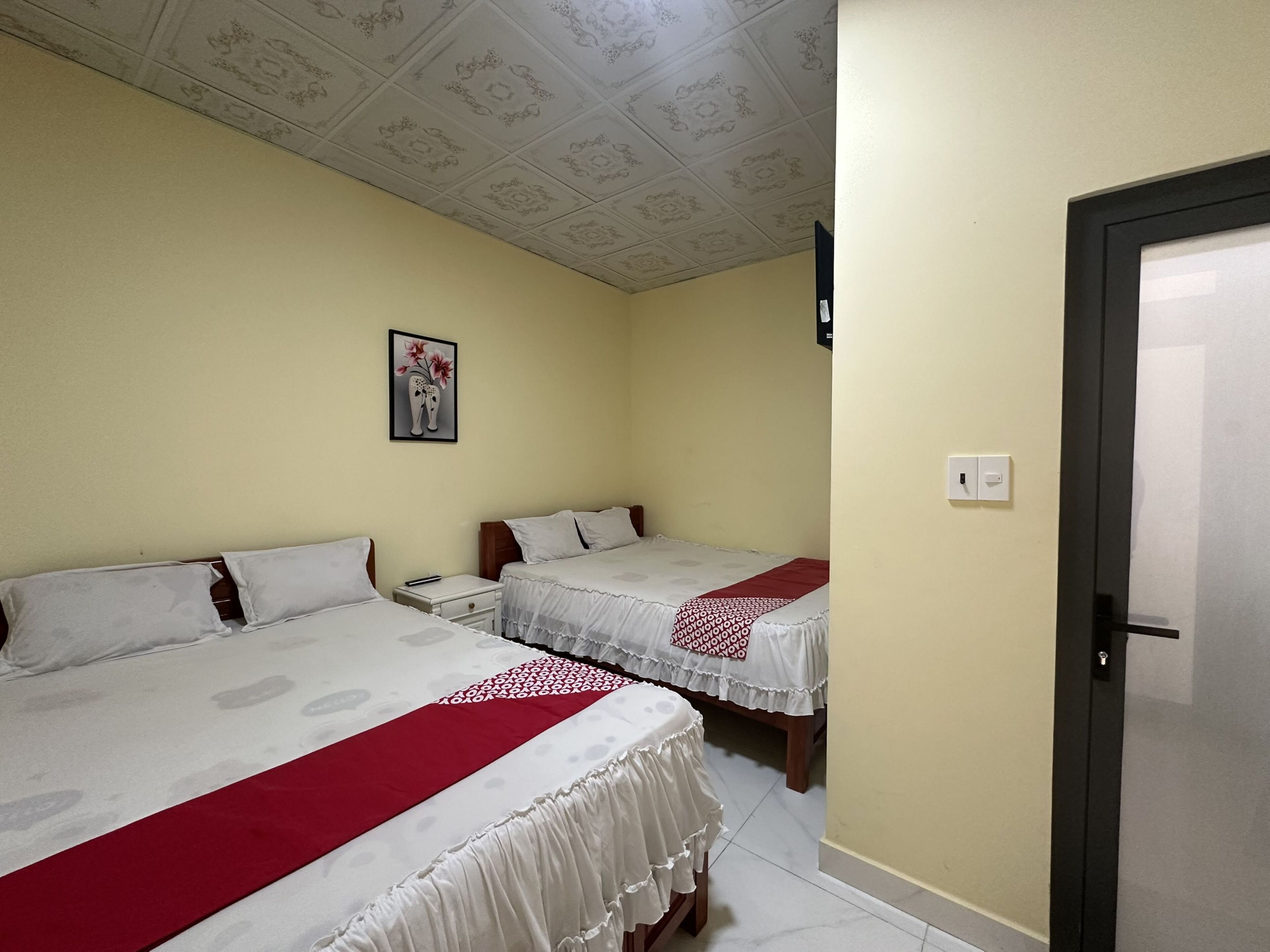 Une chambre d’hôtel avec deux lits, une petite table de chevet, un tableau encadré au mur et une porte sur le côté droit.