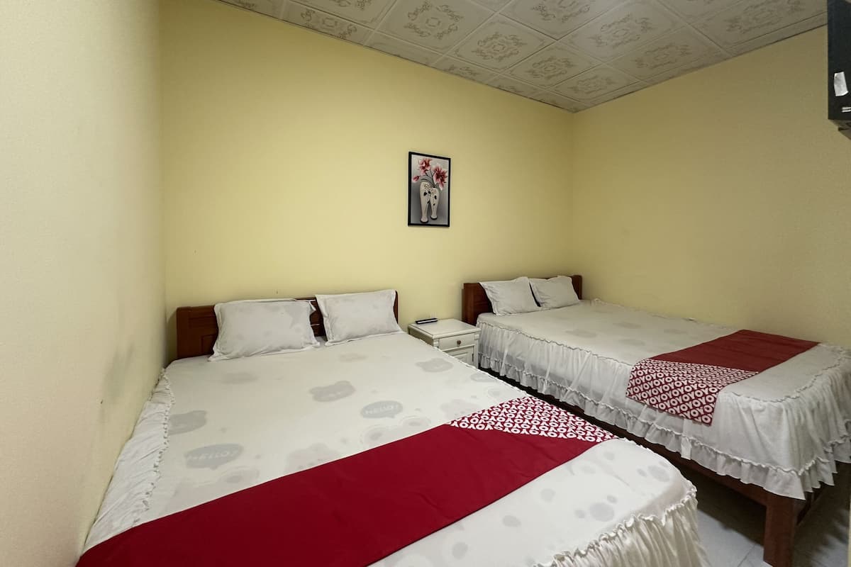 A room with two beds, each with a white bedspread and a red blanket. There is a nightstand with a lamp and a framed picture on the wall.