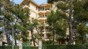 A multi-story residential building with balconies, surrounded by trees and a gated entrance. - The Blue Panoramic Penthouse (Porto Cesareo)