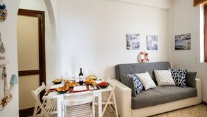 A cozy living room with a grey sofa, white table, and various food items. There are nautical-themed wall art pieces and a ceiling fan. - The Blue Panoramic Penthouse (Porto Cesareo)