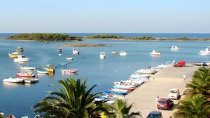 A marina with numerous boats docked, a sandy beach, and a small island in the distance. - The Blue Panoramic Penthouse (Porto Cesareo)