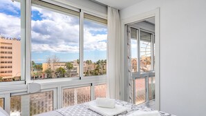 Una habitación de hotel con un ventanal grande, una cama con colcha estampada y dos toallas dobladas con cuidado.
