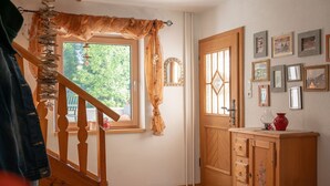 Un escalier en bois avec un rideau, une porte en bois avec un miroir et un mur orné de tableaux encadrés.