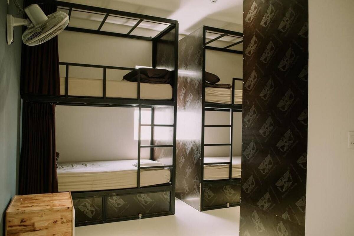 Quarto com beliche, mesa de cabeceira de madeira, ventilador de teto e papel de parede estampado.