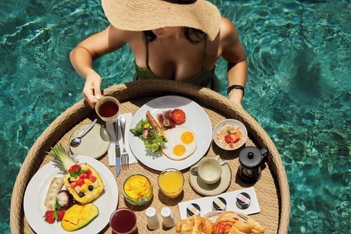 Uma pessoa de fato de banho segurando uma bandeja com itens de café da manhã, como ovos, torradas e frutas.