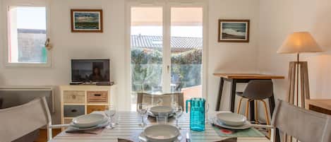 A dining area with a table set for four, a television on a stand, and a window with a view of a garden.