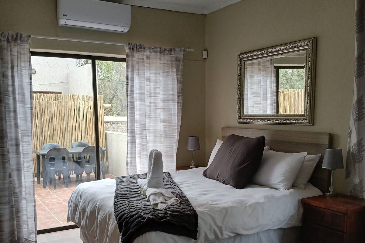 Une chambre à coucher avec un lit, une table de chevet, une lampe et une vue sur l’extérieur.