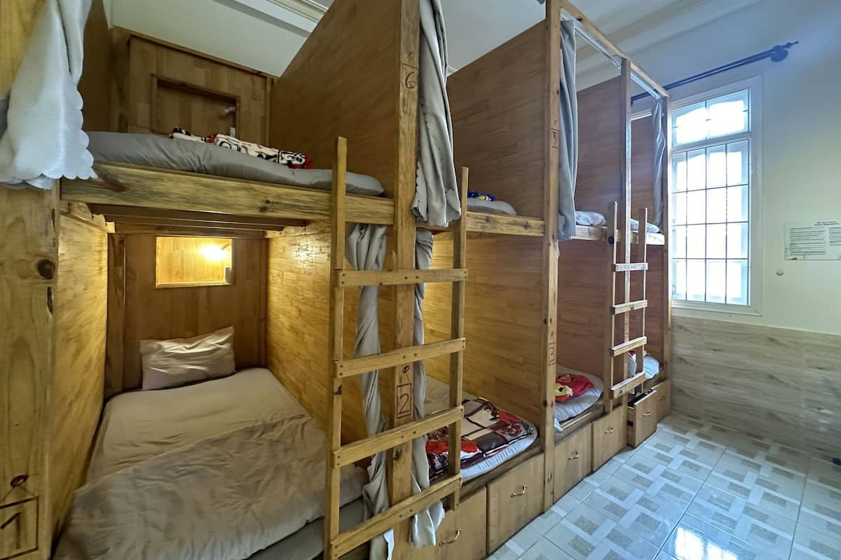 A wooden bunk bed room with a ladder, a small window, and a tiled floor.