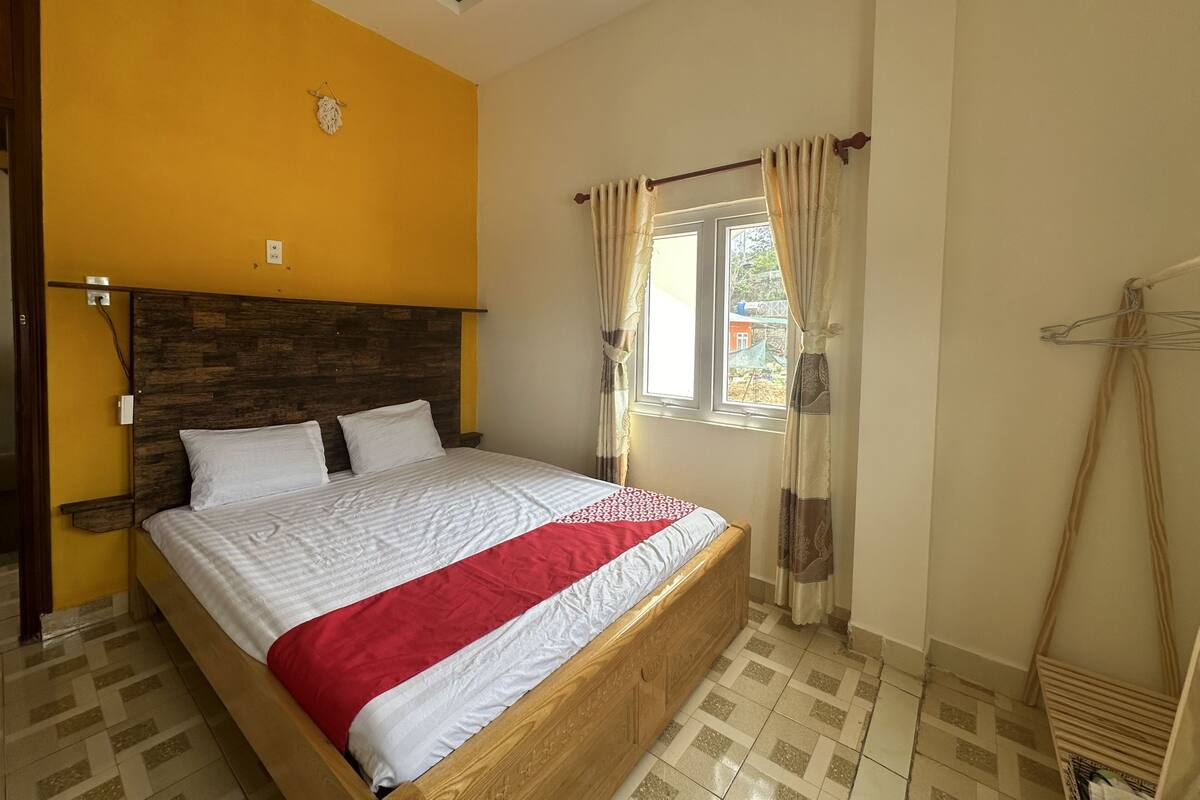 A bedroom with a wooden bed, a window with curtains, and a yellow wall.