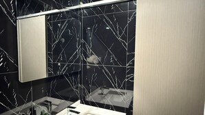 A modern bathroom with black marble walls, two sinks, and a large mirror. - Tuna Boutique Hotel (Patong)