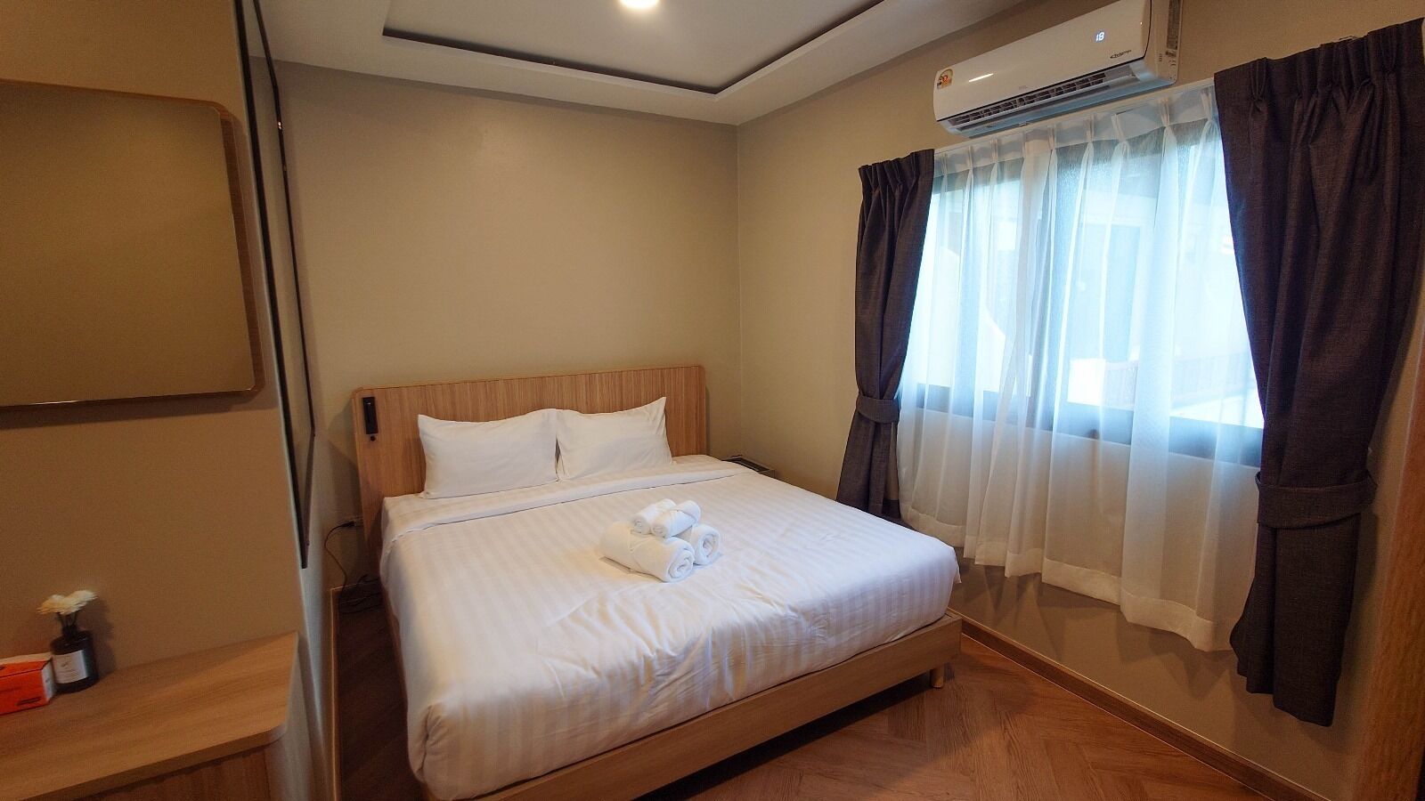 Quarto de hotel com cama, mesa de cabeceira, aparelho de ar condicionado e janela com cortinas.