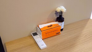 A remote control, a box labeled "Natural and comforta," and a vase with white flowers on a wooden surface. - Tuna Boutique Hotel (Patong)