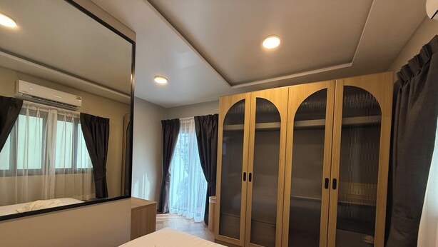 A hotel room with a large bed, a wardrobe with mirrored doors, an air conditioning unit, and a bathroom with a shower and toilet. - Tuna Boutique Hotel (Patong)