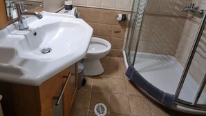 Casa de banho com lavatório, sanita e cabine de duche de vidro.