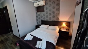 A hotel room with a bed, a nightstand, a lamp, an air conditioner, and a patterned wall. - Georgian Paradise (Kutaisi)
