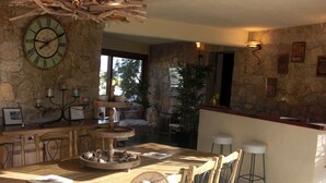 A rustic kitchen with a stone wall, wooden furniture, and a large clock. - Charmante Maison Avec Piscine et Pétanque (Lumio)