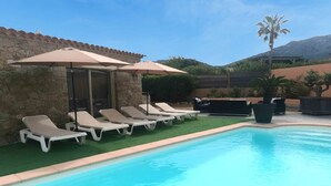 A swimming pool with lounge chairs and umbrellas, surrounded by stone walls and greenery. - Charmante Maison Avec Piscine et Pétanque (Lumio)