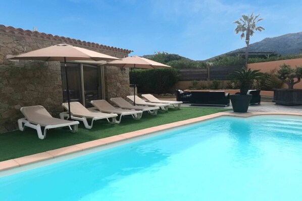 A swimming pool with lounge chairs and umbrellas, surrounded by stone walls and greenery. - Charmante Maison Avec Piscine et Pétanque (Lumio)