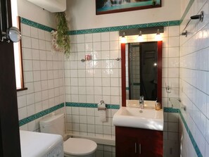 A bathroom with white tiles, a white toilet, a sink with a mirror, and a shower area. - Charmante Maison Avec Piscine et Pétanque (Lumio)