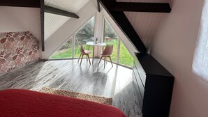 Ein Schlafzimmer mit Schrägdecke, einem großen Fenster, einem Essbereich mit Stühlen und einem roten Teppich.