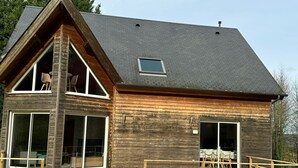 Ein modernes, zweistöckiges Haus mit großen Fenstern, einem geneigten Dach und einer Holzfassade.