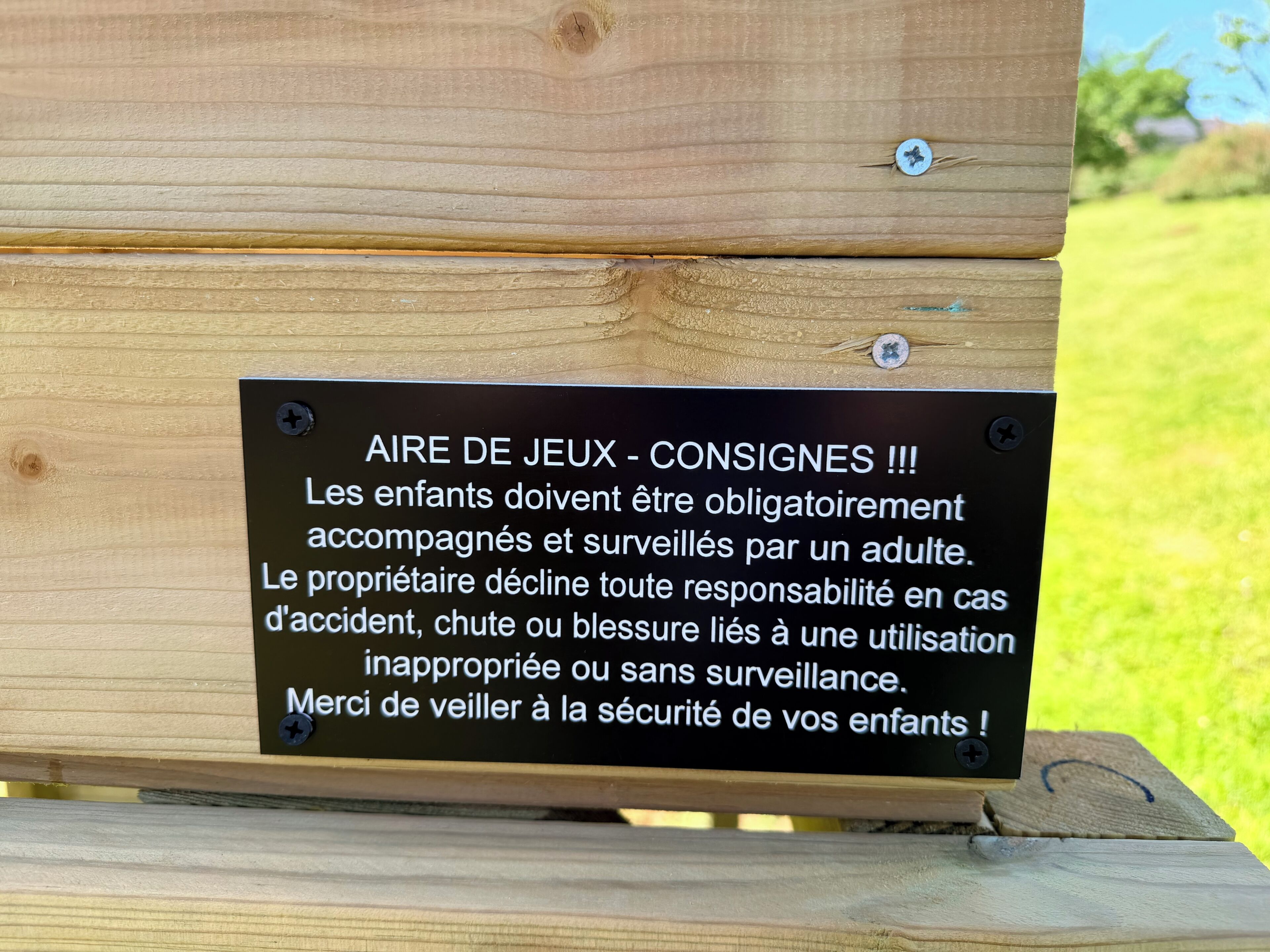 Une pancarte sur une structure en bois, avec un texte en français, avertit de la nécessité d’une surveillance parentale des enfants dans l’aire de jeux.