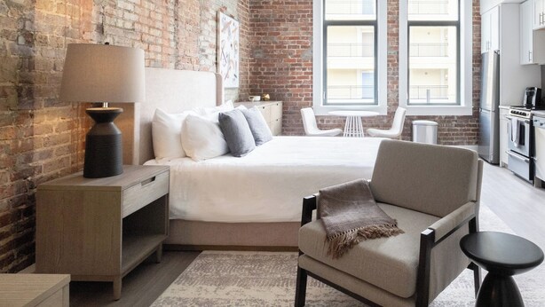 Un dormitorio con cama, mesita de noche, lámpara y una silla.