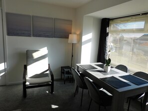 A hotel room with a dining table, chairs, a lamp, a potted plant, and artwork on the wall.