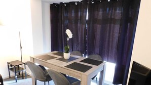 Un coin repas comprenant une table, des chaises, une plante en pot et un rideau.