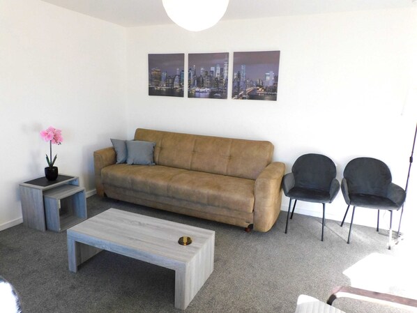 A living room with a sofa, two chairs, a coffee table, a small side table with a flower, and three cityscape paintings on the wall.