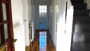 Un couloir doté d’un plancher en bois, d’une porte blanche et d’un escalier dont les marches sont recouvertes d’une moquette sombre.