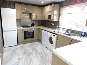 A compact kitchen with a refrigerator, oven, microwave, washing machine, and a sink.