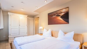 Hotellihuone, jossa on suuri sänky, yöpöytä, seinään kiinnitetty lamppu ja maalaus, jossa on kuvattuna rantamaisema.