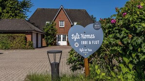 A heart-shaped sign for Slyt Homes EBBE & FLUT with a QR code and a small heart logo. - Hier Lautet das Motto: Wohnen und Entspannen mit Heimat-atmosphäre (Westerland)