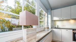 Una cocina moderna con armarios blancos, encimera de mármol y un amplio ventanal con vistas a un jardín.