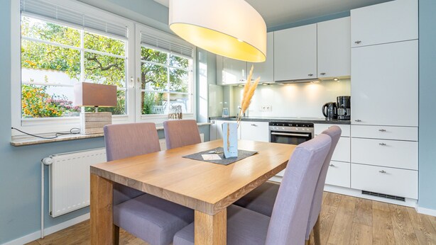 Una cocina moderna con armarios blancos, una mesa de comedor de madera y una lámpara colgante.