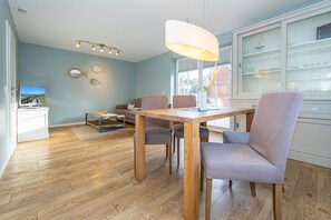 Relax in this stylish living room with a dining table, comfortable seating for four, and a mounted TV.