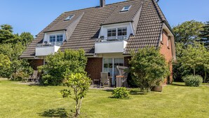 A two-story house with a sloped roof, a balcony, and a well-maintained lawn. - Hier Lautet das Motto: Wohnen und Entspannen mit Heimat-atmosphäre (Westerland)