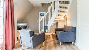Een moderne woonkamer met een trap, een flatscreen televisie en twee grijze banken.