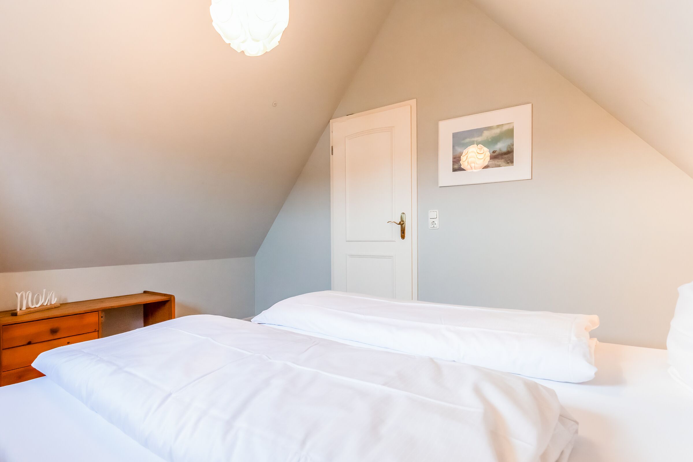 Ein Schlafzimmer mit zwei Betten, einem Holznachttisch, einer weißen Tür und einem gerahmten Bild an der Wand.