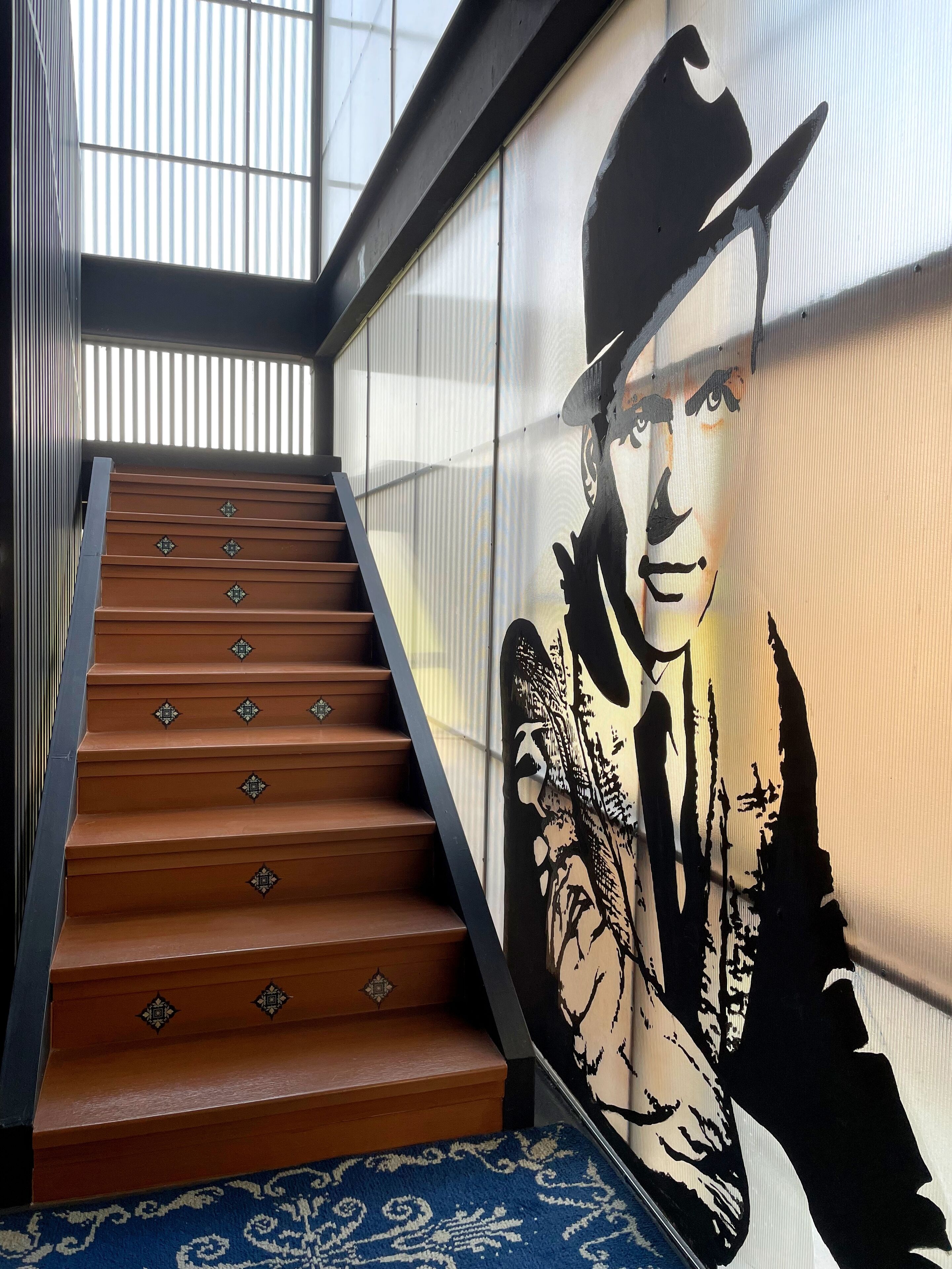 A staircase with wooden steps and decorative diamond patterns, leading to a room with a large window and a wall mural.