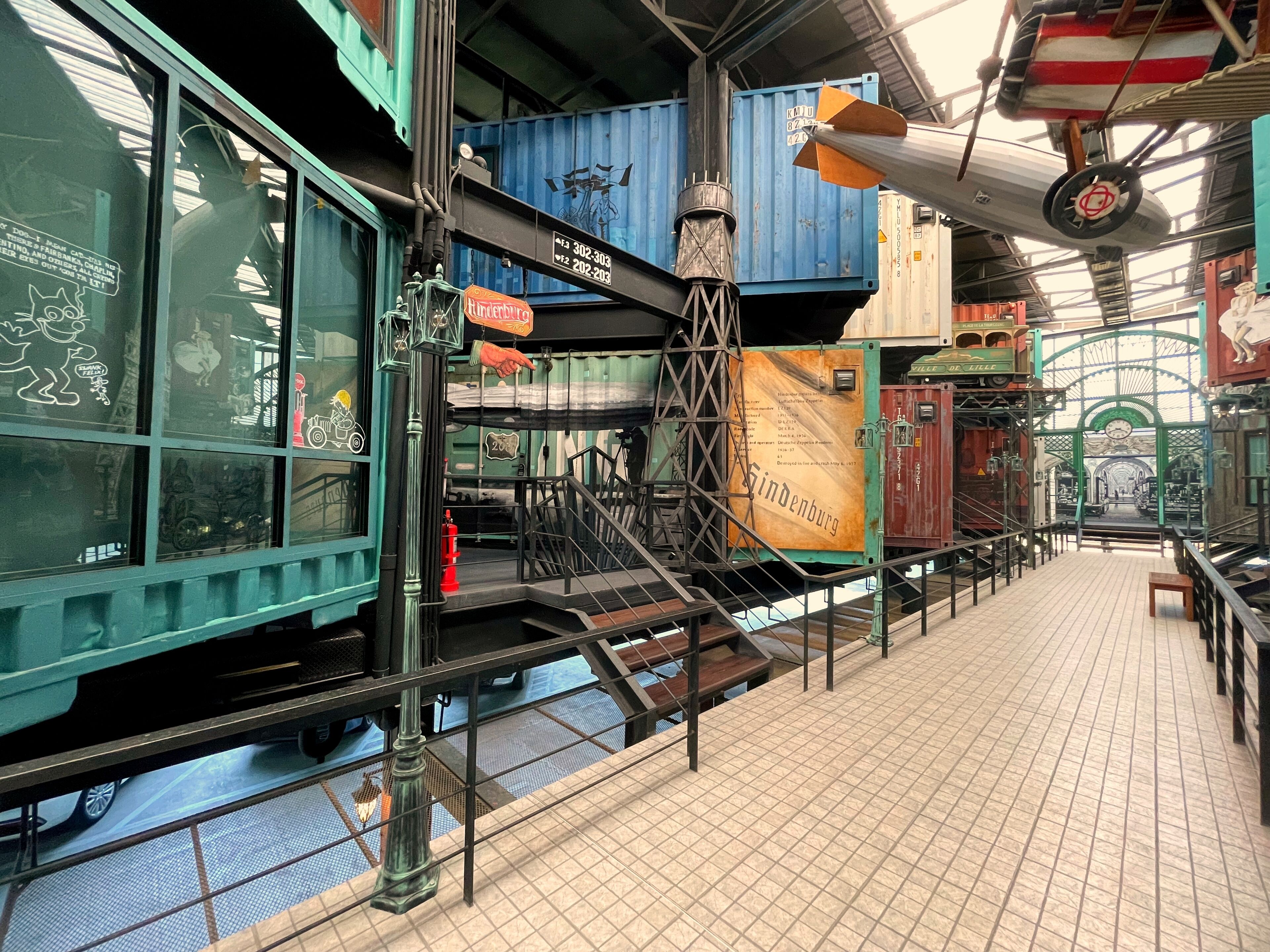 A train station platform with multiple train carriages, a staircase, and a tiled floor.
