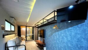 A modern room with a bed, a desk, a chair, a TV, and a blue textured wall. - Nights in a Box (Chonburi)