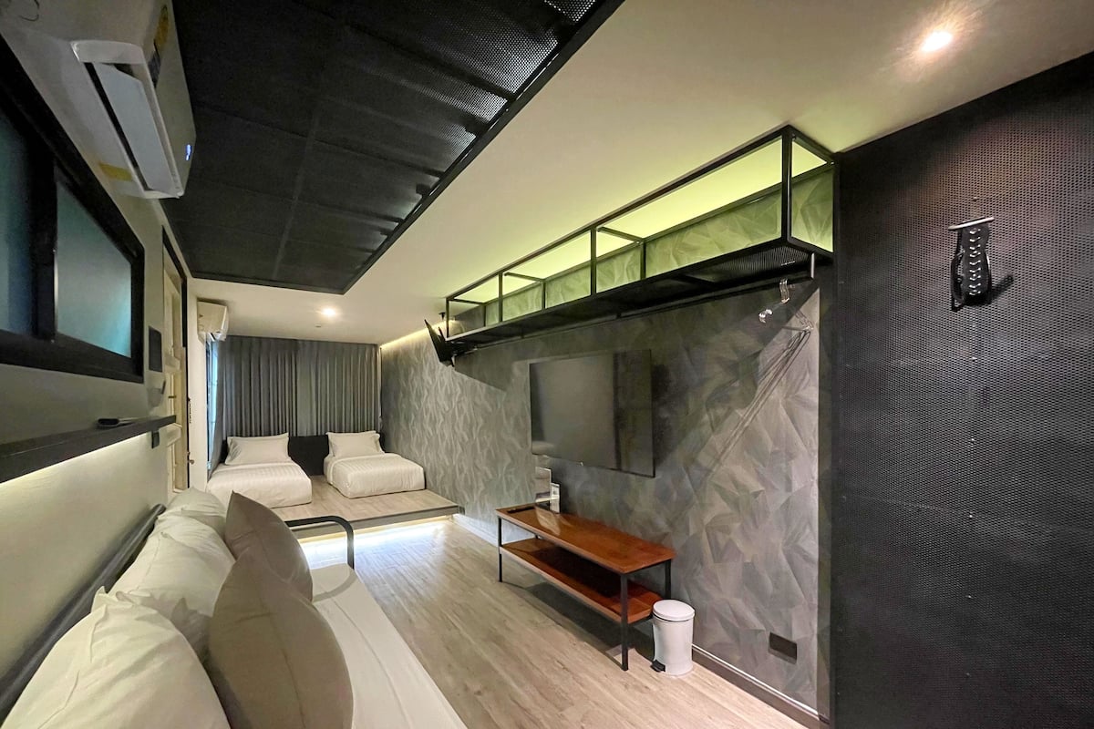A modern, compact bedroom with a bunk bed, a small seating area, and a large mirror on the wall.