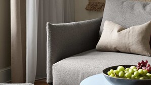 Ett modernt vardagsrum med en grå soffa, ett runt soffbord och en skål med druvor.