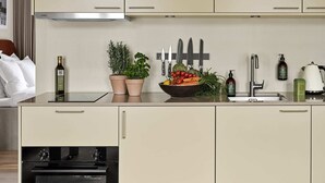 Ett modernt kök med beige skåp, en svart bänkskiva och ett stort utbud av färska grönsaker och frukter.